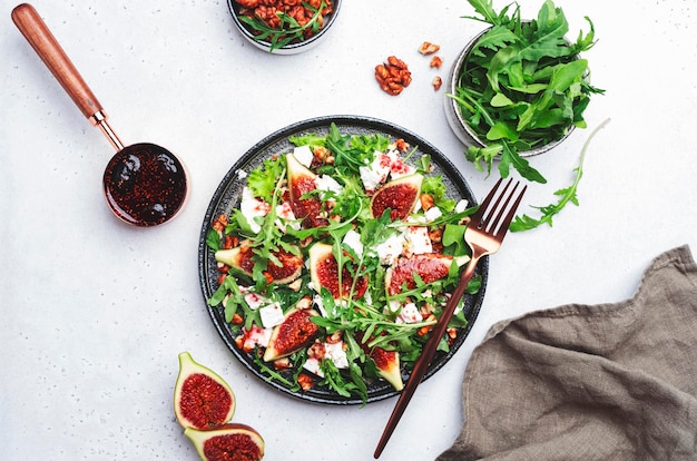 Delicious summer salad with sweet figs white feta cheese walnuts arugula and jam vinegar dressing on white table background top view negative space