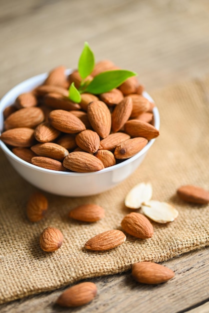 Delicious sweet almonds on the wooden table roasted almond nut for healthy food and snack Almonds nuts on white bowl and green leaf on sack background