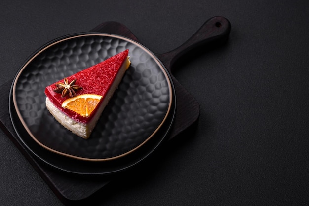 Delicious sweet cheesecake with raspberry jam on a black ceramic plate on a dark concrete background