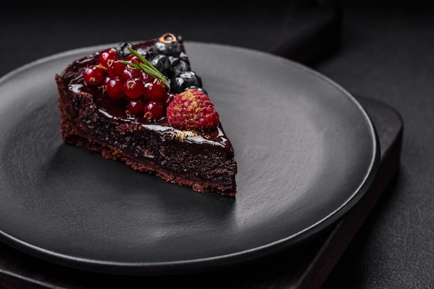 Вкусный сладкий шоколадный торт с черникой, смородиной и малиной на керамической тарелке