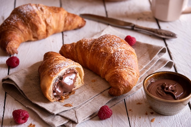 Delicious sweet croissant with chocolate and fruit on white wooden table