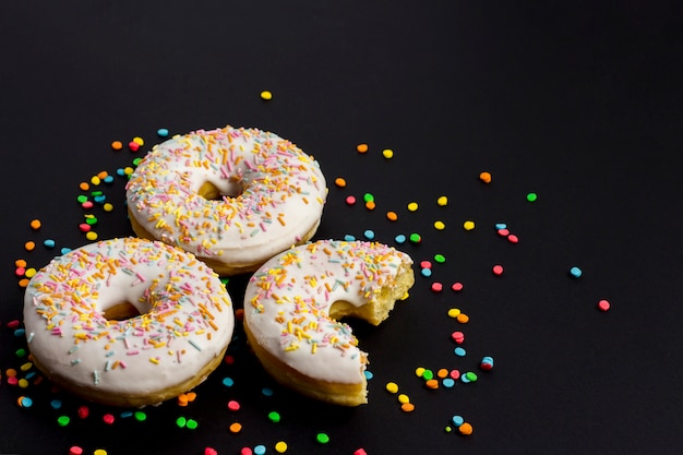 Delicious, sweet, fresh donuts and multicolored decorative candies on a black background. Breakfast concept, fast food, coffee shop, bakery.