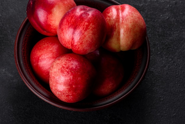 Delicious sweet peaches or nectarines in a brown bowl on a dark concrete background