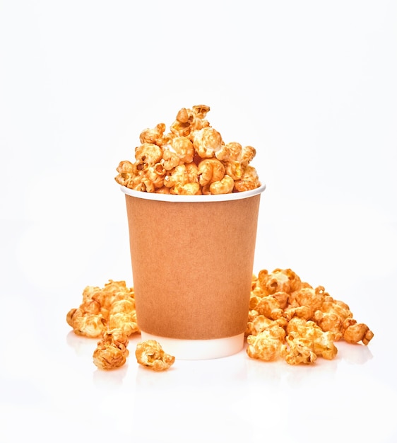 Delicious sweet popcorn with caramel in simple paper cup, isolated on white table.