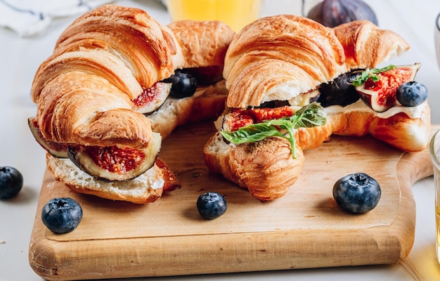 Delicious sweet sandwich with croissants soft cheese blueberries and figs on marble backdrop Breakfast concept with coffee and oranfe juice Selective focus