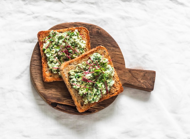 Foto delici tapas aperitivo spuntino bruschetta con uova di avocado cetrioli verdi sparsi su una tavola da taglio in legno su uno sfondo chiaro