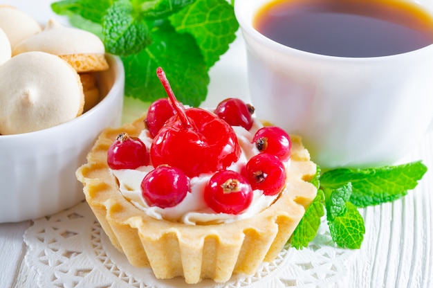 Delicious tartlet with fresh berries and cream cheese, a cup of tea and small cookies.