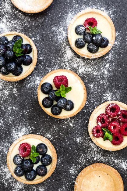 Delicious tartlets with raspberries and blueberries on black