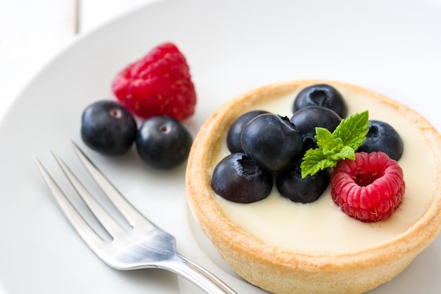 Delicious tartlets with raspberries and blueberries on white wooden table