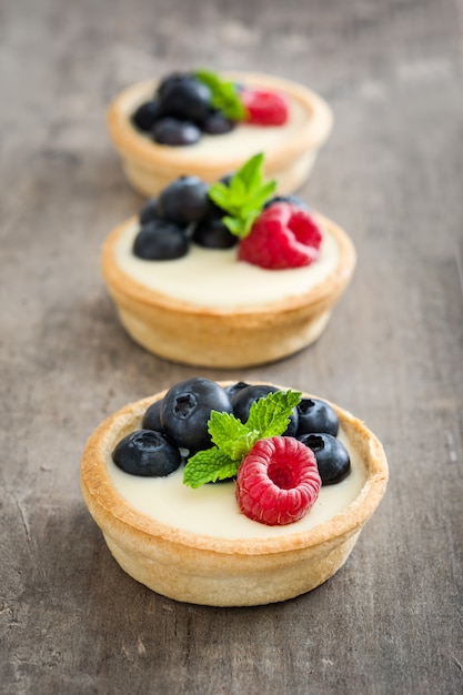 Delicious tartlets with raspberries and blueberries on a wooden table