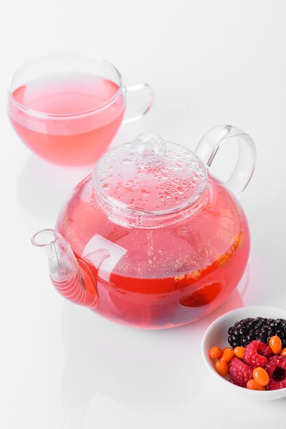 Delicious tea of berries and fruits in a beautiful glass teapot on a white background with reflection. Morning Tea Party