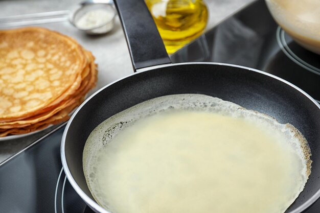 Delicious thin pancake in frying pan on induction stove closeup