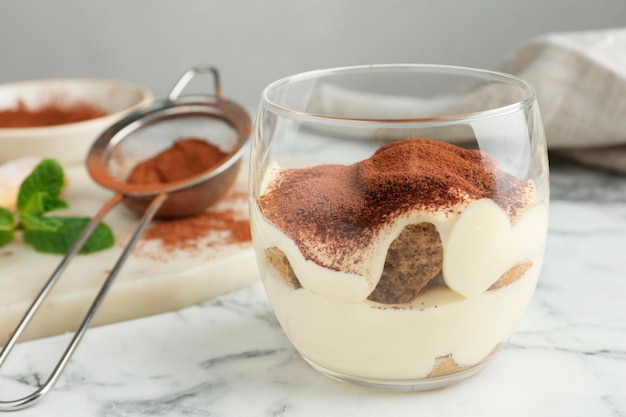 Вкусное тирамису в бокалах и сито с какао-порошком на белом мраморном столе вблизи