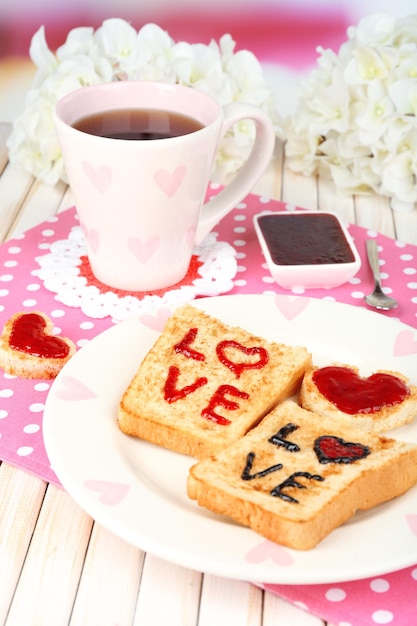 Delicious toast with jam and cup of tea on table close-up