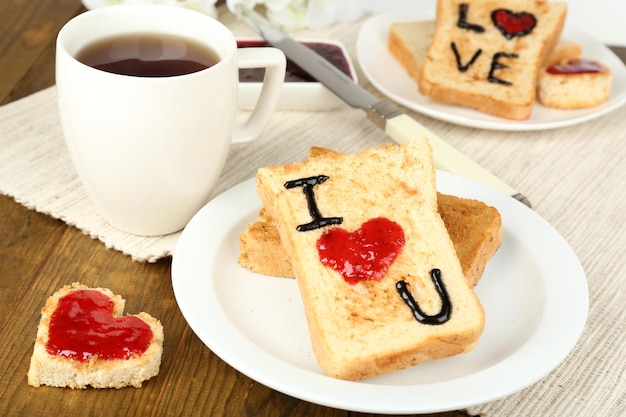 Delicious toast with jam and cup of tea on table close-up