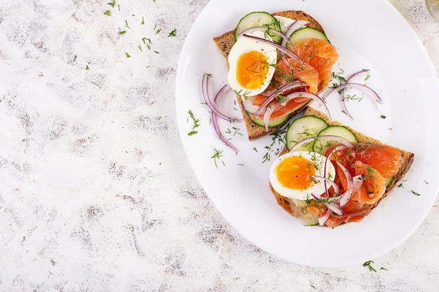 Delicious toast with salmon boiled egg cucumber and cream cheese on a white plate Healthy eating breakfast Keto diet food Tasty food Top view