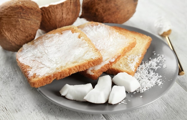 Delicious toasts with coconut oil in plate on table closeup