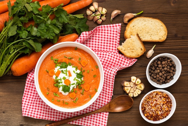 Delicious traditional carrot soup with herbs and sour cream on a wooden table.