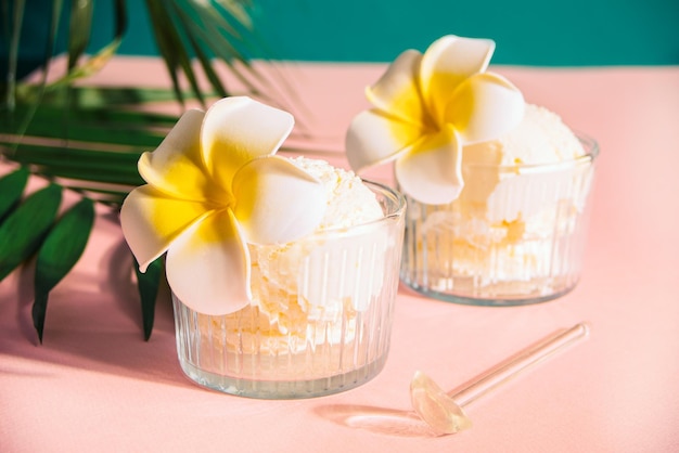 Delicious tropical flavors ice cream sorbet sundae decorated flower plumeria frangipani and palm leaf on the background Summer food concept