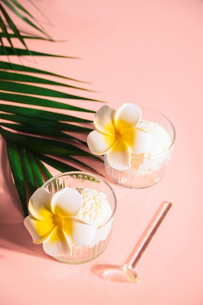 Delicious tropical flavors ice cream sorbet sundae decorated flower plumeria frangipani and palm leaf on the background Summer food concept