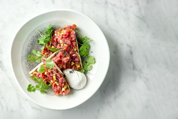 Deliziosa tartare di tonno con avocado, coriandolo, servita su crostini di segale in un piatto bianco con uovo in camicia. spuntino di cucina giapponese