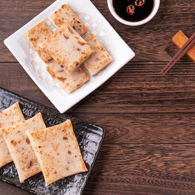 Delicious turnip cake Chinese traditional local radish cake in restaurant with soy sauce and chopsticks close up copy space top view flat lay