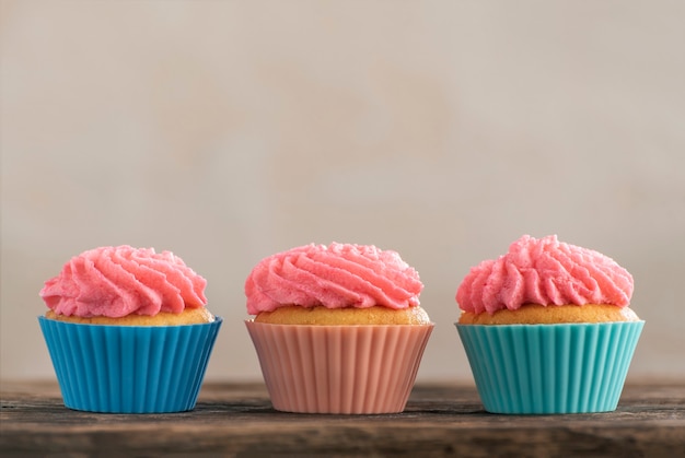 Delicious vanilla mousxes with pink cream. Three homemade muffins on wooden. Copy space. Birthday cupcake on light background.