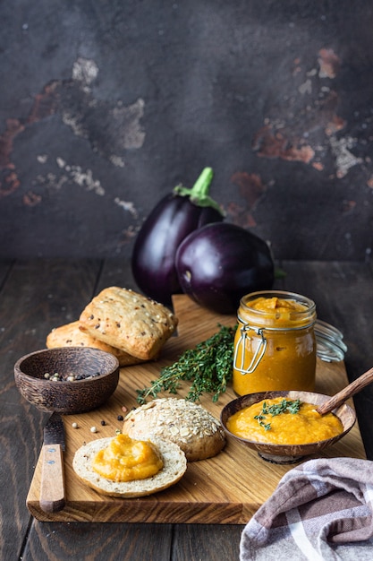 Il delizioso caviale di verdure in una ciotola e un barattolo di legno è servito con pane multicereali.