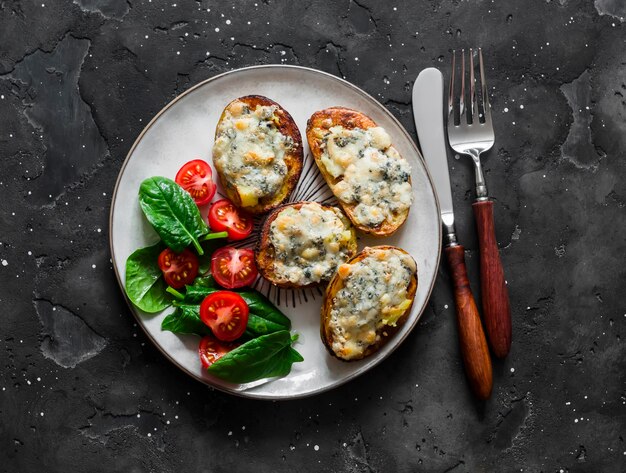 Delicious vegetarian lunch roasted potatoes with gorgonzola and fresh vegetable salad on a dark background top view