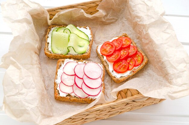 Delicious vegetarian sandwiches with cream cheese fresh cucumber radish tomatoes in a wicker basket