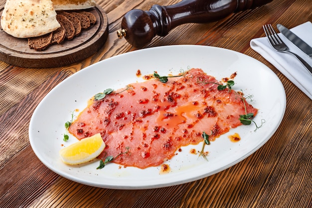Delicious view on tuna carpaccio on white plate. Close up view on Raw tuna tenderloin with sauce on wooden background with copy space. Fresh italian appetizer. Seafood italian mediterranean cuisine