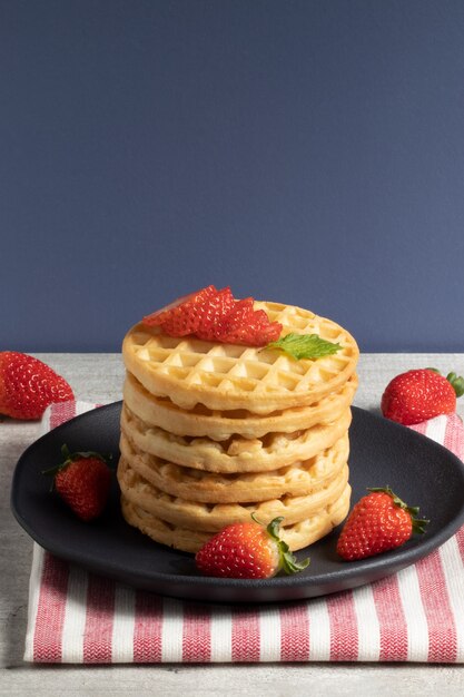 Delicious waffles and strawberries on black plate.