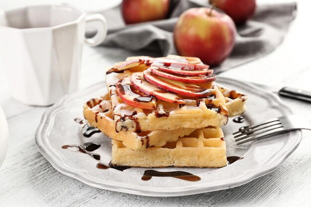 Delicious waffles with apple slices syrup and sugar powder on plate