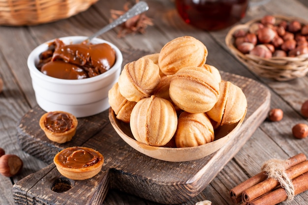 Deliziosi biscotti a forma di noce ripieni di latte condensato dolce e noci su un vecchio tavolo di legno, primo piano