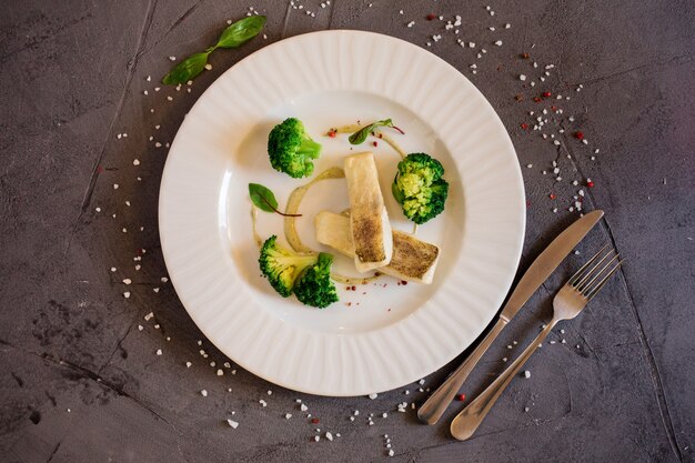 Delicious white fish served on the white plate on the grey background. Restourant menu.