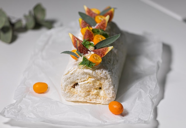 Delicious white meringue cake with cream decorated with kumquat mint figs on parchment paper