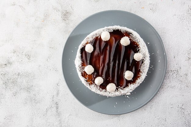 Delicious whole chocolate cake on plate with coconut candies on top on table on marble background. Wallpaper for pastry cafe or cafe menu. horizontal.