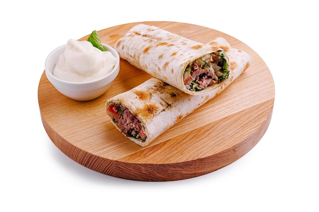 Вкусный оберток с приправленным мясом и свежими овощами, подаваемый с кремовым соусом на деревянной тарелке