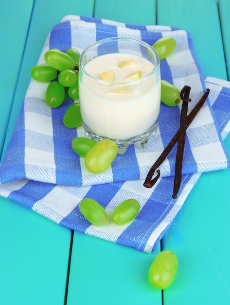 Delicious yogurt in glass with grapes on wooden table closeup