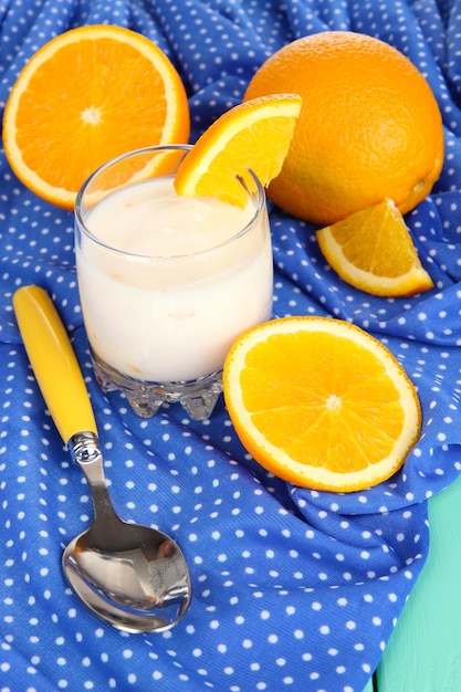 Delicious yogurt in glass with orange on blue tablecloth