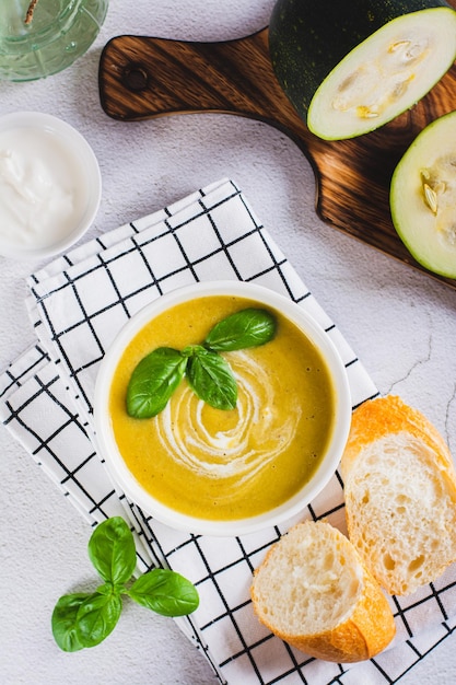 Delicious zucchini soup puree in a bowl and pieces of bread on the table top and vertical view