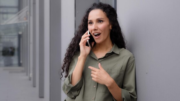 Delight Latin Hispanic gelukkig lachend succes vrouw in de buurt van gebouw buiten praten telefoon goed nieuws