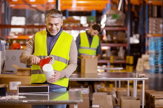 Delighted adult man putting stickers on the bottle while working in the warehouse