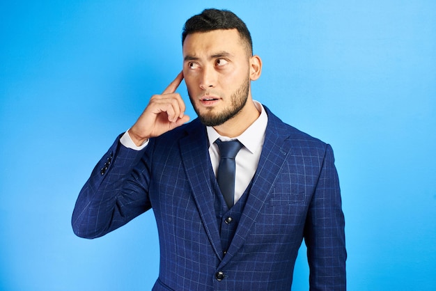 Delighted asian kazakh businessman has an idea, raised index
finger with open mouth in a suit and tie in blue studio
isolated