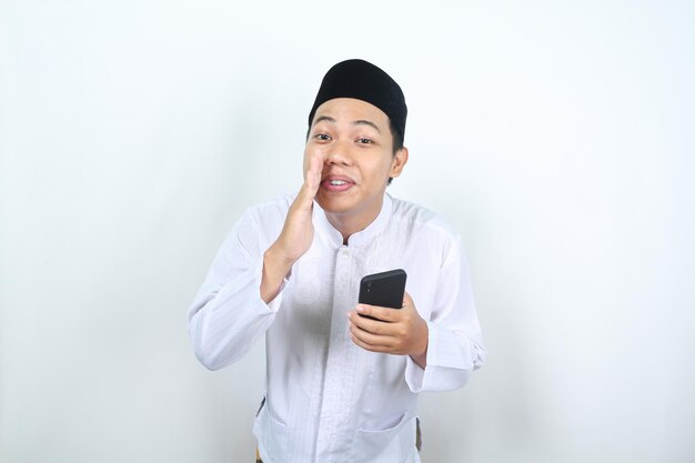 사진 기하는 아시아 무슬림 남자가 휴대전화를 들고 속삭이는 몸짓을 한다.