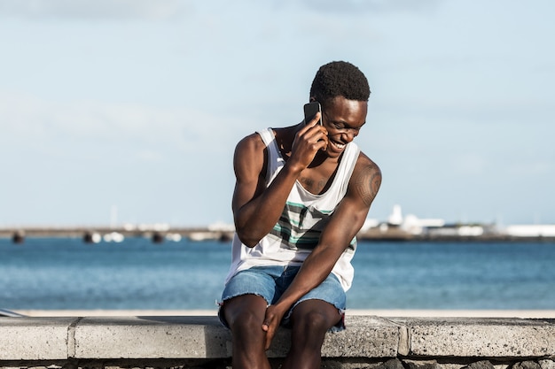 Delighted black man talking on smartphone on embankment