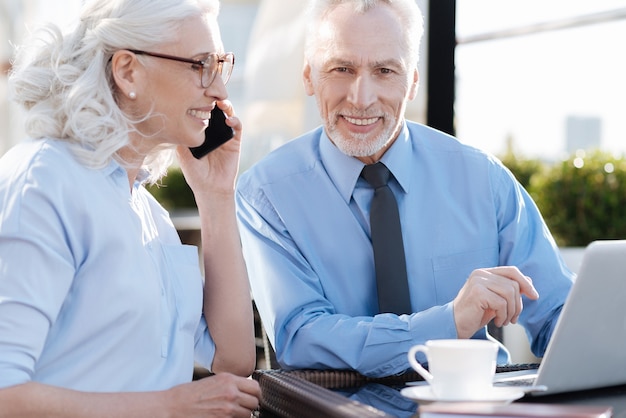 Photo delighted blonde keeping smile on her face and holding telephone near left ear while sitting in semi position