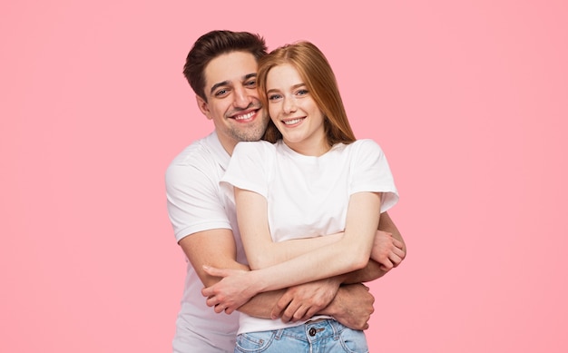 Delighted couple hugging and looking at camera on pink background