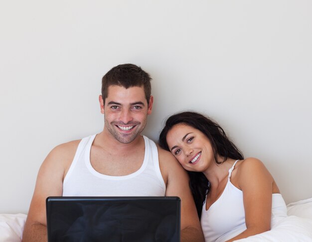 Delighted couple sitting on the bed with laptop