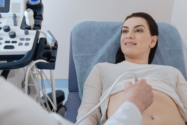 Delighted emotional young lady looking excited while paying attention to every word the expert saying while performing an ultrasound